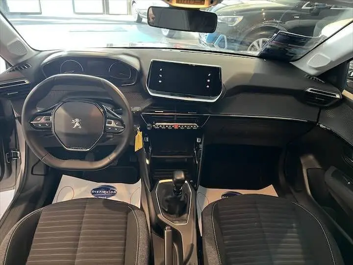 Vue intérieure avant du Peugeot 208 gris Artense, montrant le volant compact, écran tactile et levier de vitesse manuel.