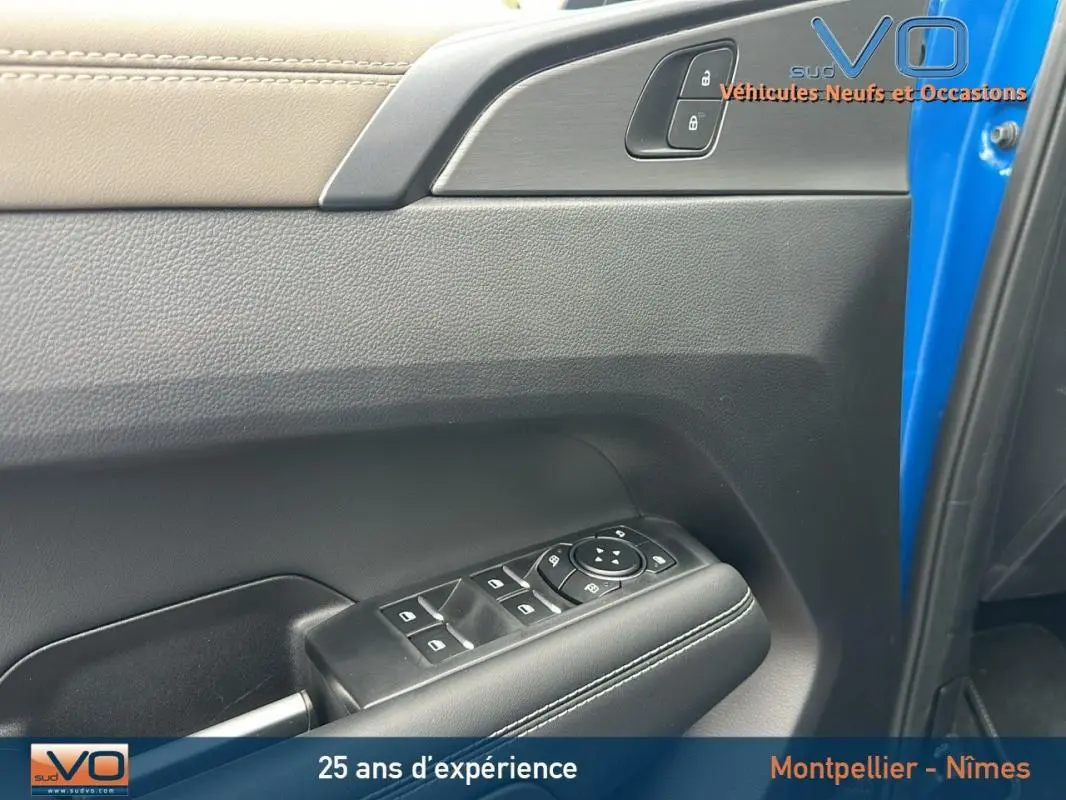 Vue rapprochée de la porte côté conducteur bleu du Volkswagen Amarok 2025, avec commandes de vitres et verrouillage.