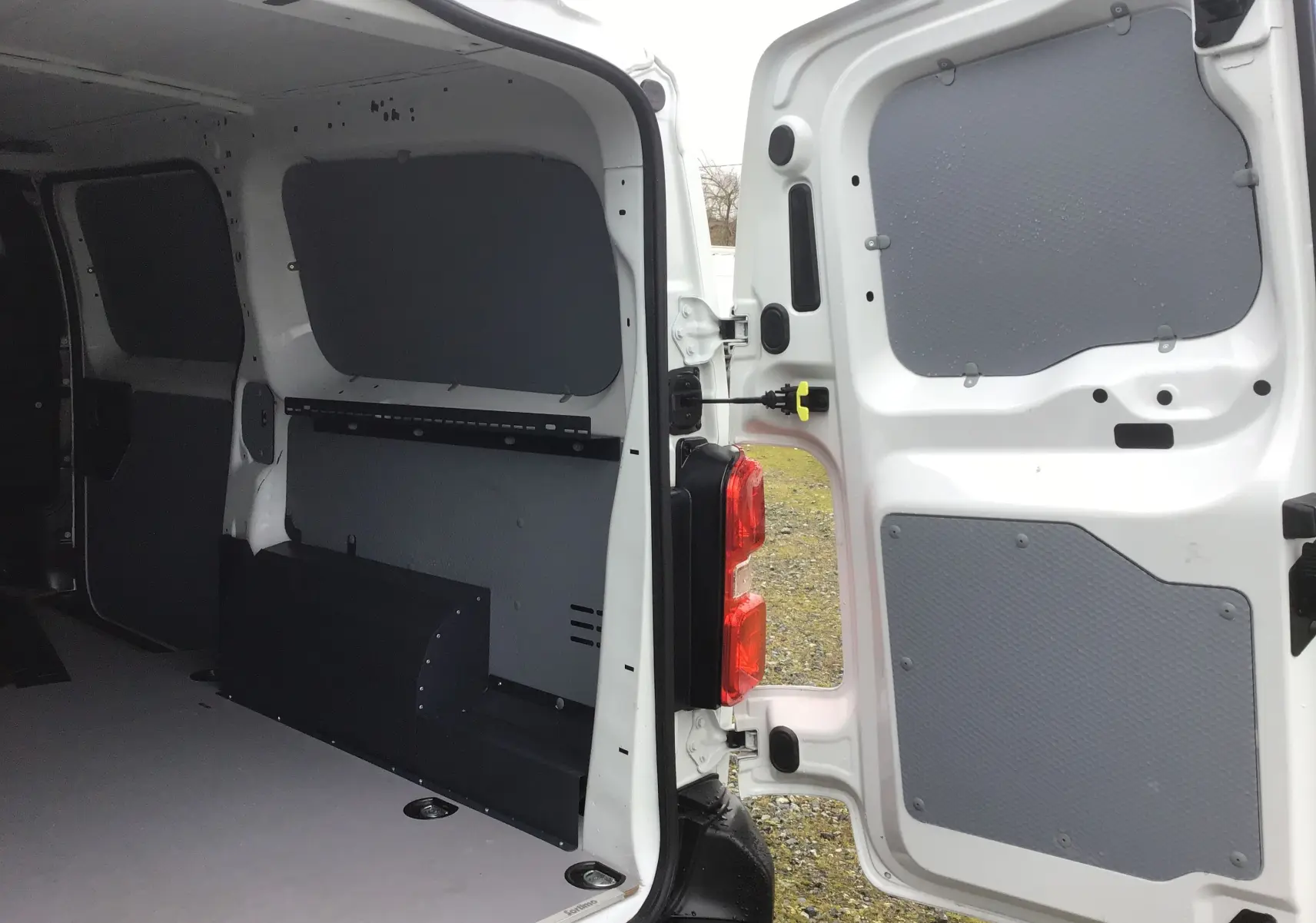 Vue intérieure arrière du FIAT Scudo Fourgon blanc 2024 avec portes ouvertes, montrant l'aménagement utilitaire et les panneaux de protection gris.