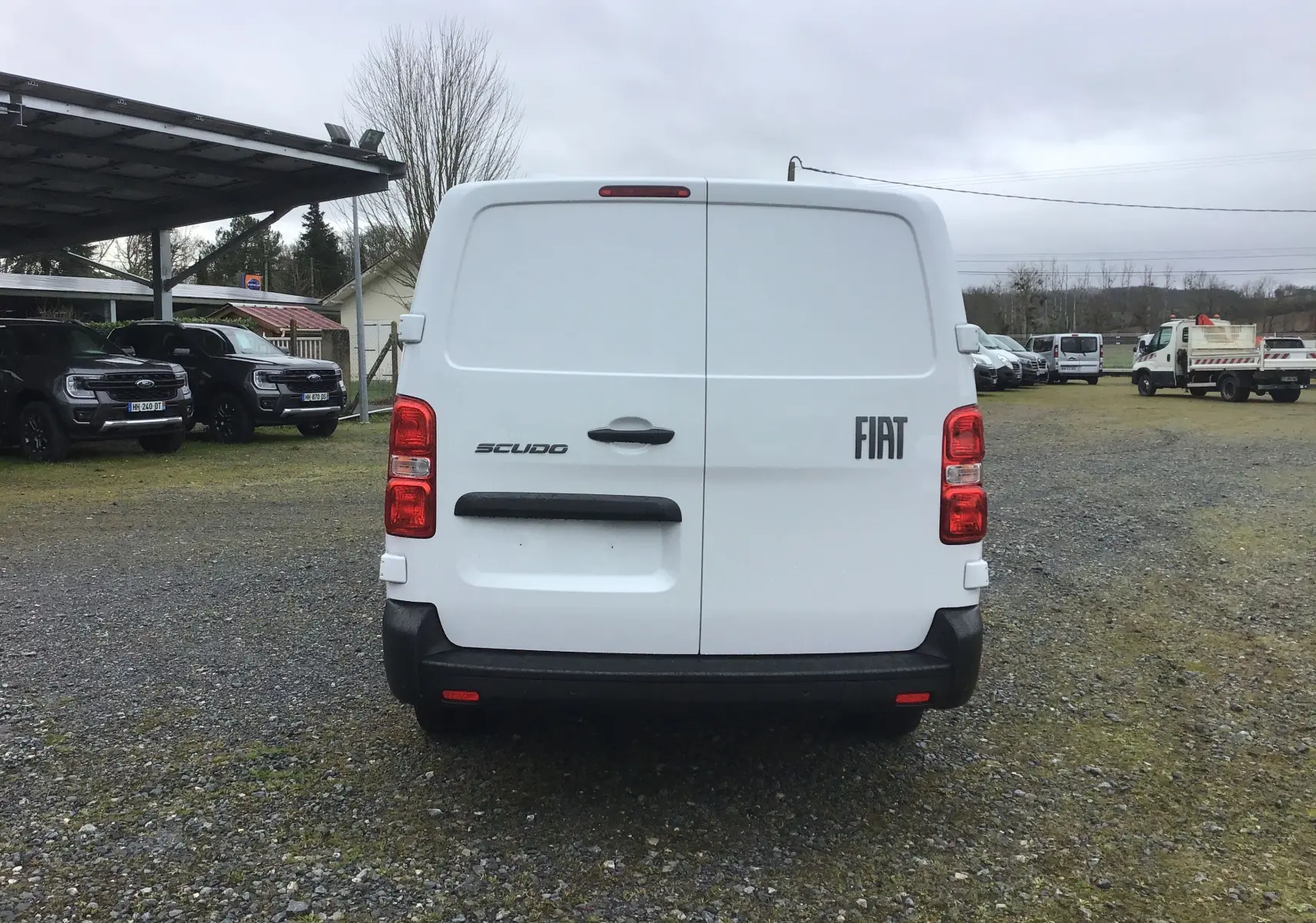 Vue arrière d’un FIAT Scudo Fourgon blanc 2024 avec portes battantes et feux arrière rouges sur un terrain extérieur.