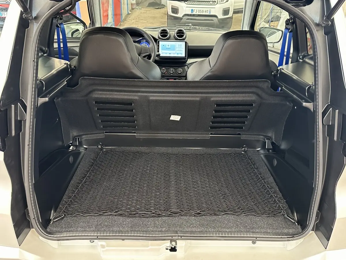 Vue arrière ouverte sur le coffre d'une Aixam Ambition 0.5 City GTO blanc, avec intérieur noir et sièges avant visibles.