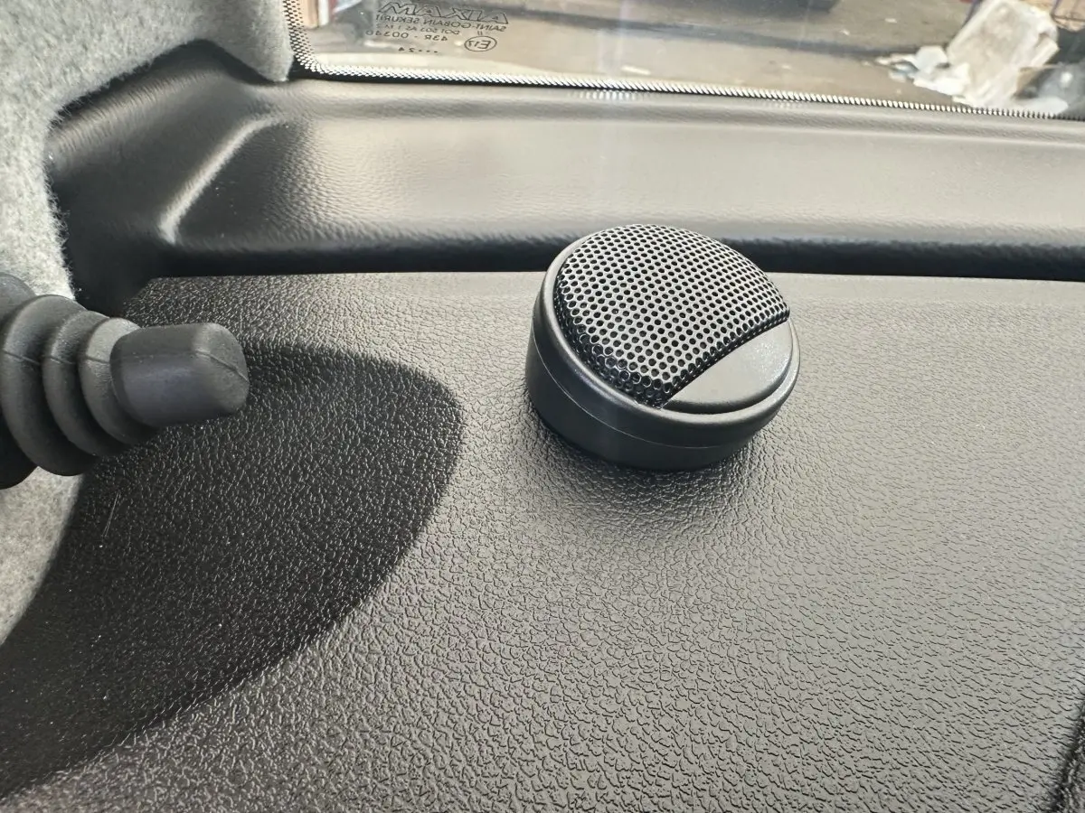 Gros plan sur un haut-parleur noir intégré au tableau de bord texturé d’une Aixam Ambition 0.5 City GTO blanche.