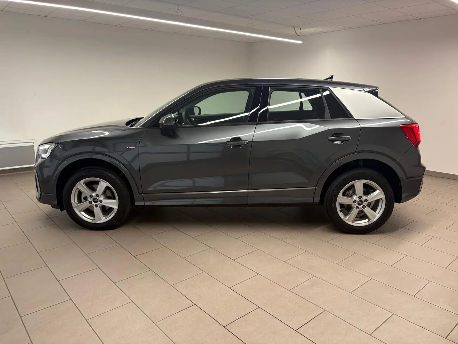 Vue de profil côté gauche d'un Audi Q2 35 TFSI S Line gris Daytona métallisé dans un intérieur neutre.