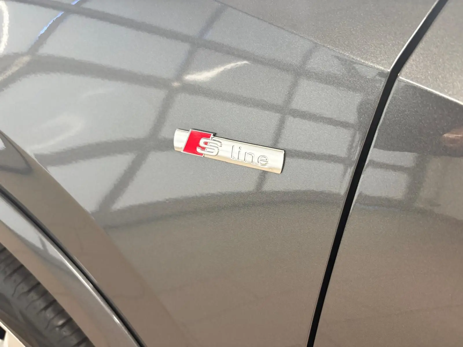 Gros plan sur l'emblème S line sur l'aile avant droite d'un Audi Q2 gris Daytona métallisé.