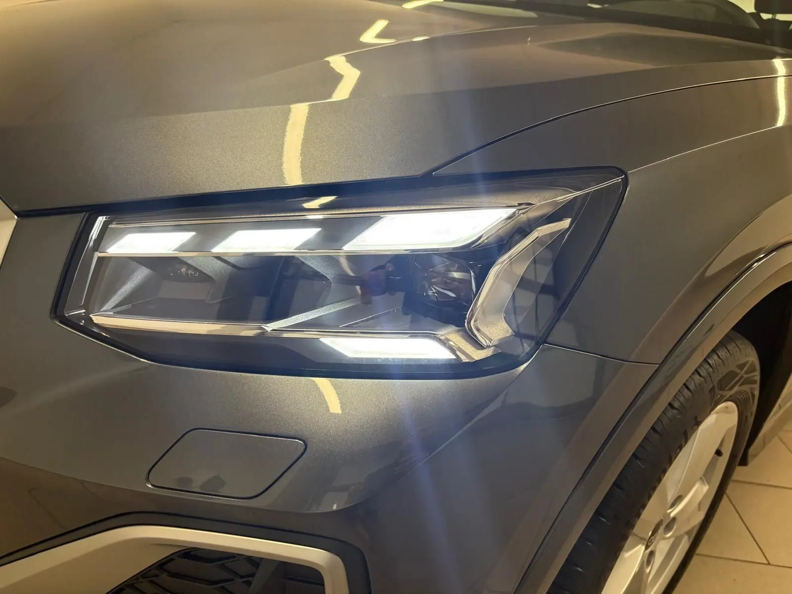Gros plan sur le phare avant droit allumé de l'Audi Q2 35 TFSI S Line en gris Daytona métallisé.