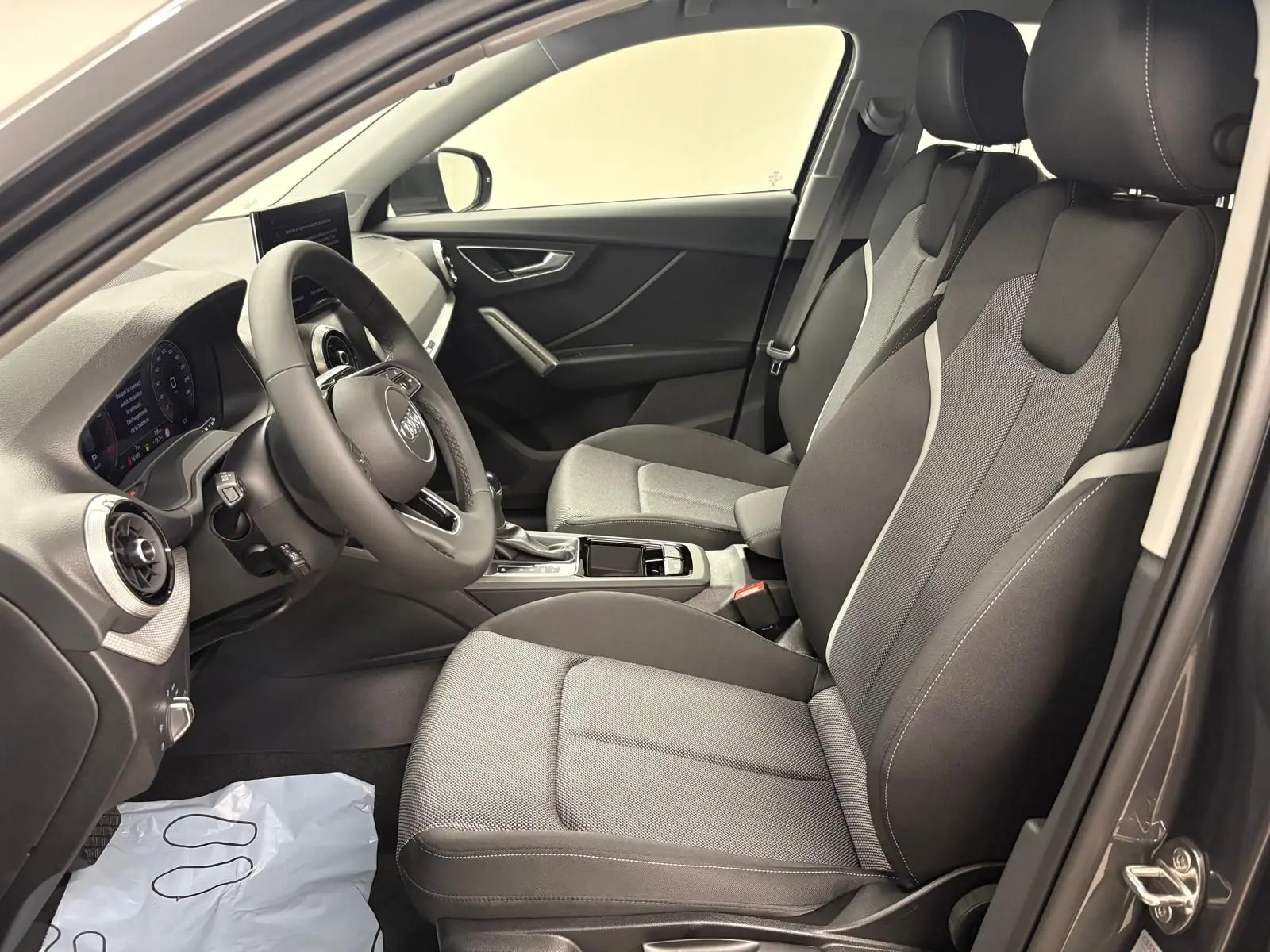 Vue intérieure côté conducteur de l'Audi Q2 35 TFSI S Line 2026, sièges tissu gris et tableau de bord moderne.