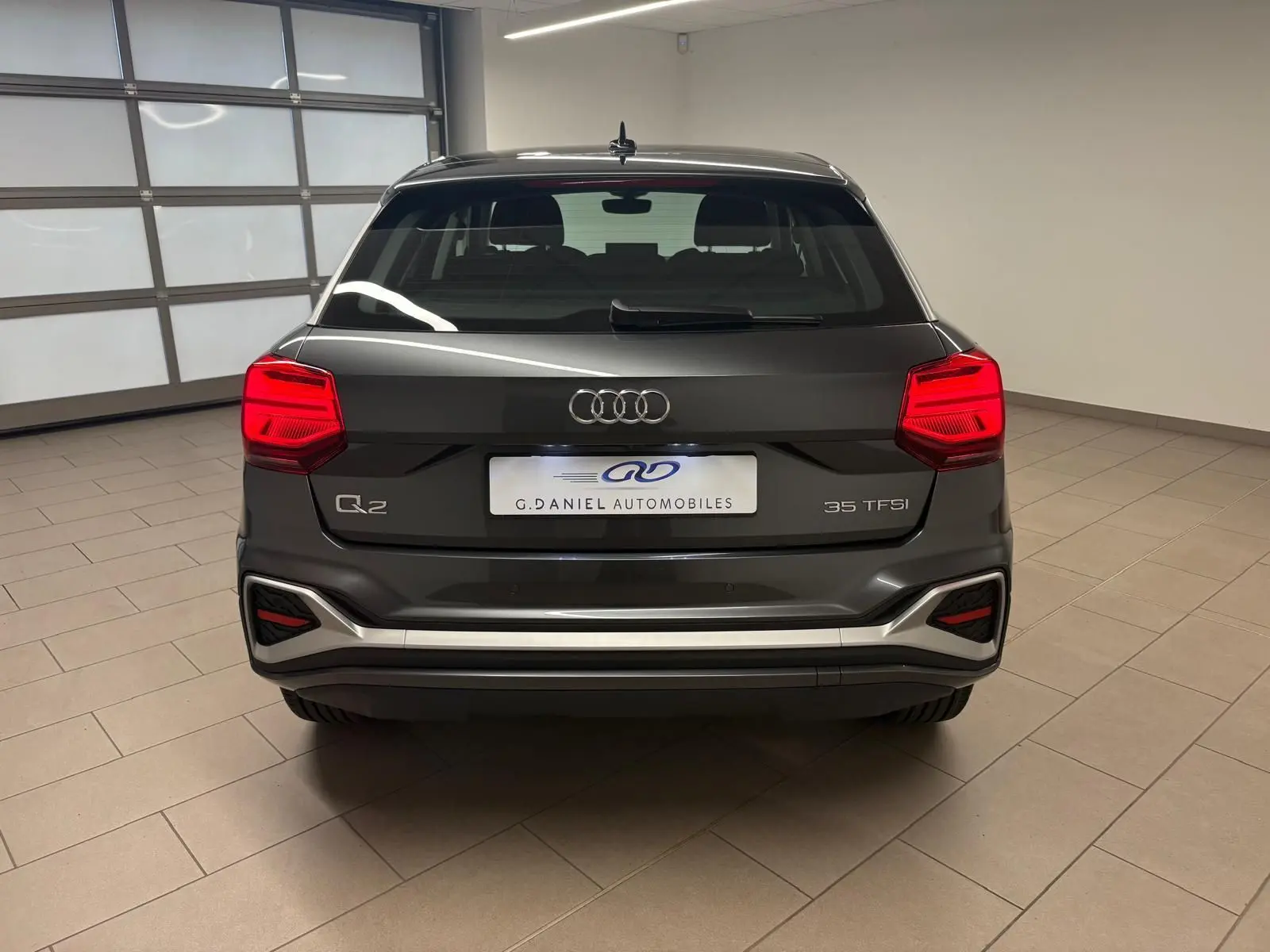 Vue arrière d'un Audi Q2 35 TFSI gris Daytona avec feux rouges allumés dans un garage lumineux.