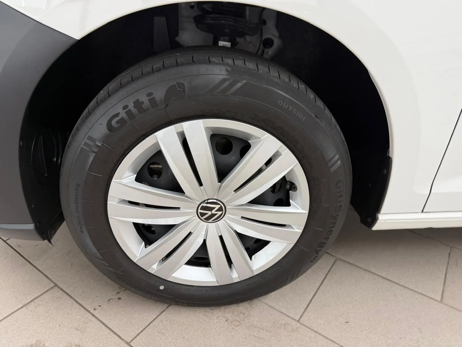 Gros plan sur la roue avant droite blanche du Volkswagen Caddy 2.0 TDI 122 DSG7 Business avec enjoliveur argenté.