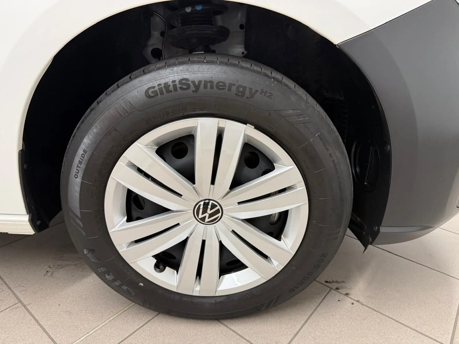 Gros plan sur la roue avant droite blanche du Volkswagen Caddy 2.0 TDI 122 DSG7 Business avec enjoliveur argenté.