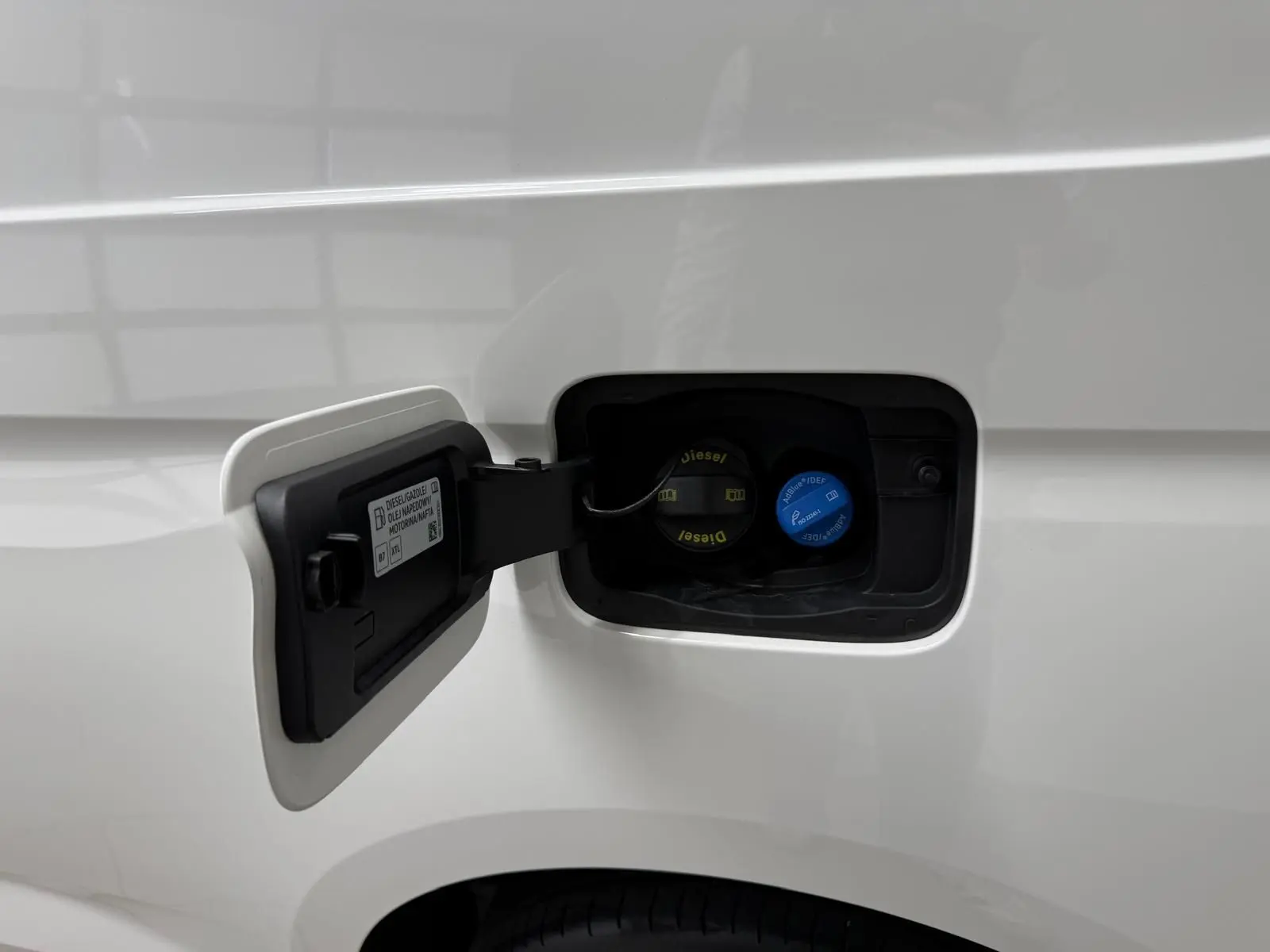 Détail de la trappe à carburant ouverte sur un Volkswagen Caddy blanc candy, avec bouchons diesel et AdBlue visibles.