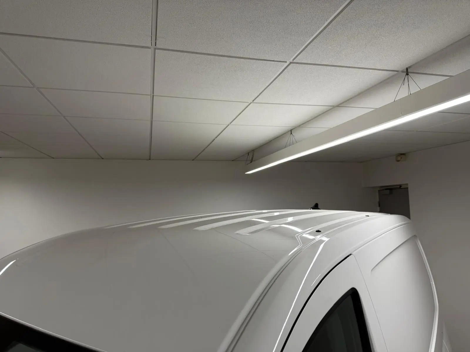 Toit blanc candy du Volkswagen Caddy 2.0 TDI 122 DSG7 Business vu en léger angle depuis l'arrière droit dans un garage.