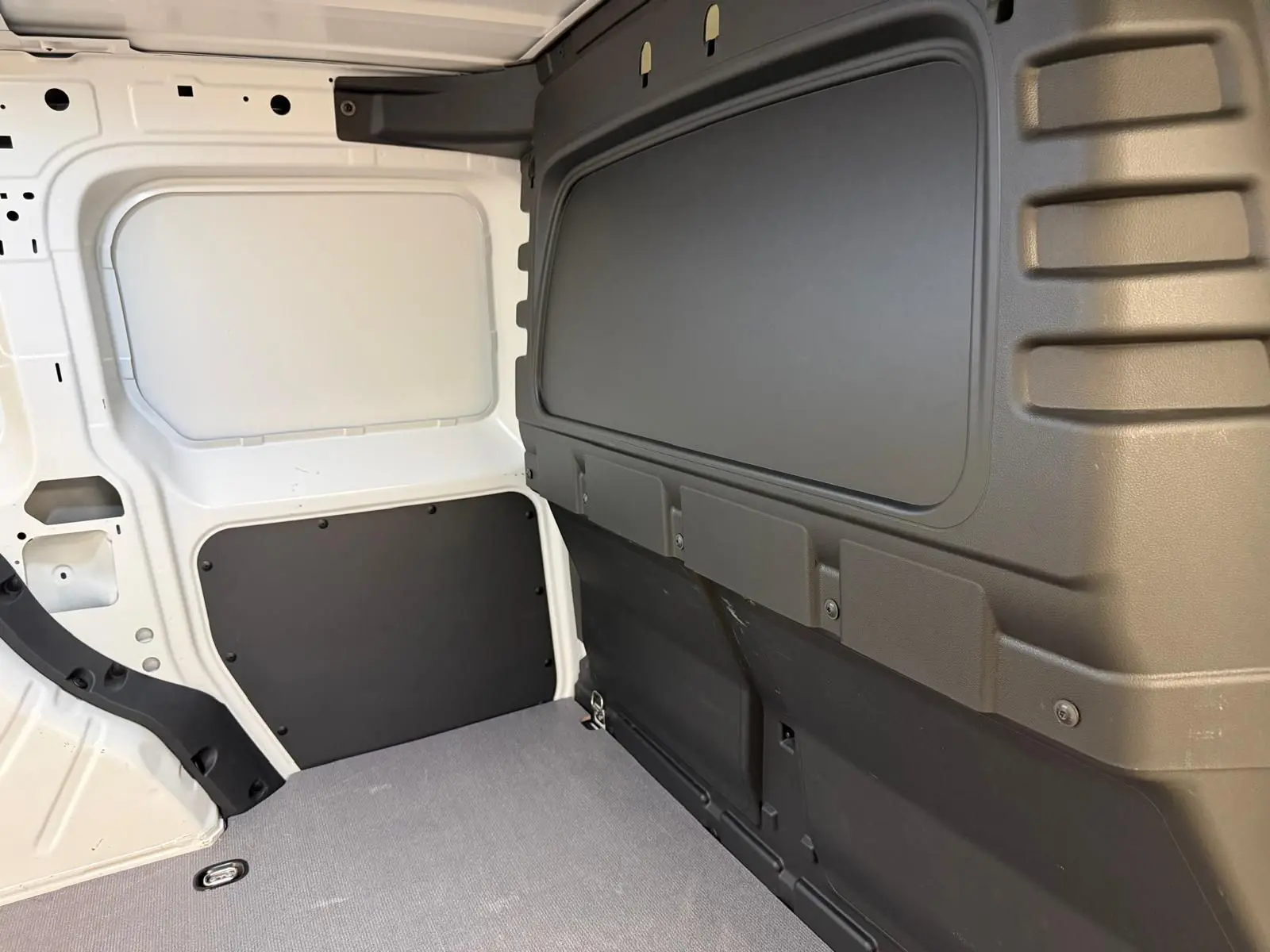 Vue intérieure du compartiment de charge du Volkswagen Caddy blanc Candy, avec parois et plancher protégés en plastique noir.