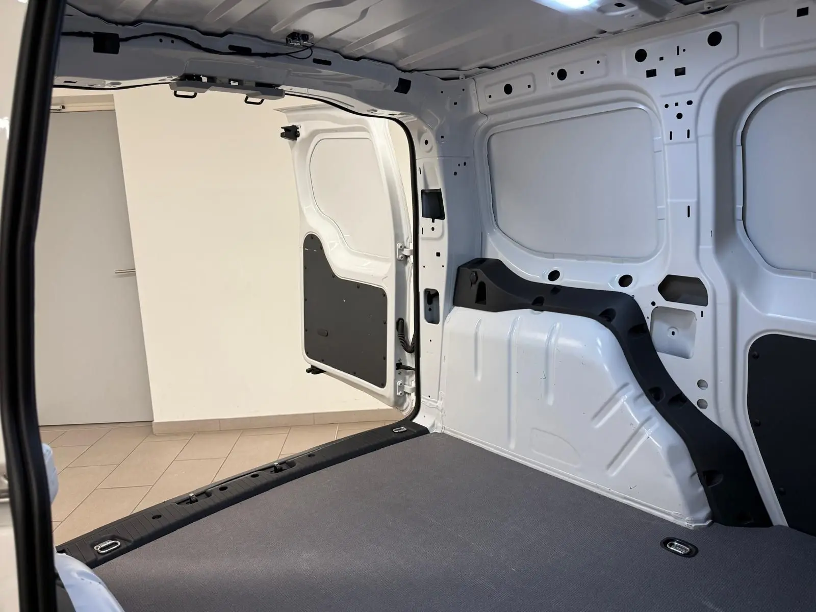 Vue intérieure arrière du Volkswagen Caddy blanc Candy 2025, montrant le compartiment de charge vide et la porte battante ouverte.