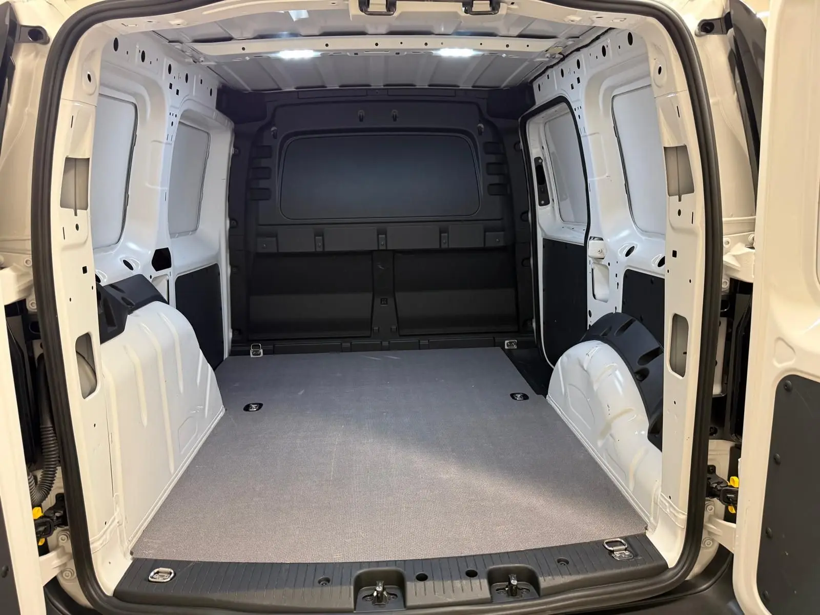 Vue intérieure arrière du Volkswagen Caddy blanc Candy 2025, montrant l'espace de chargement vide et les parois métalliques.