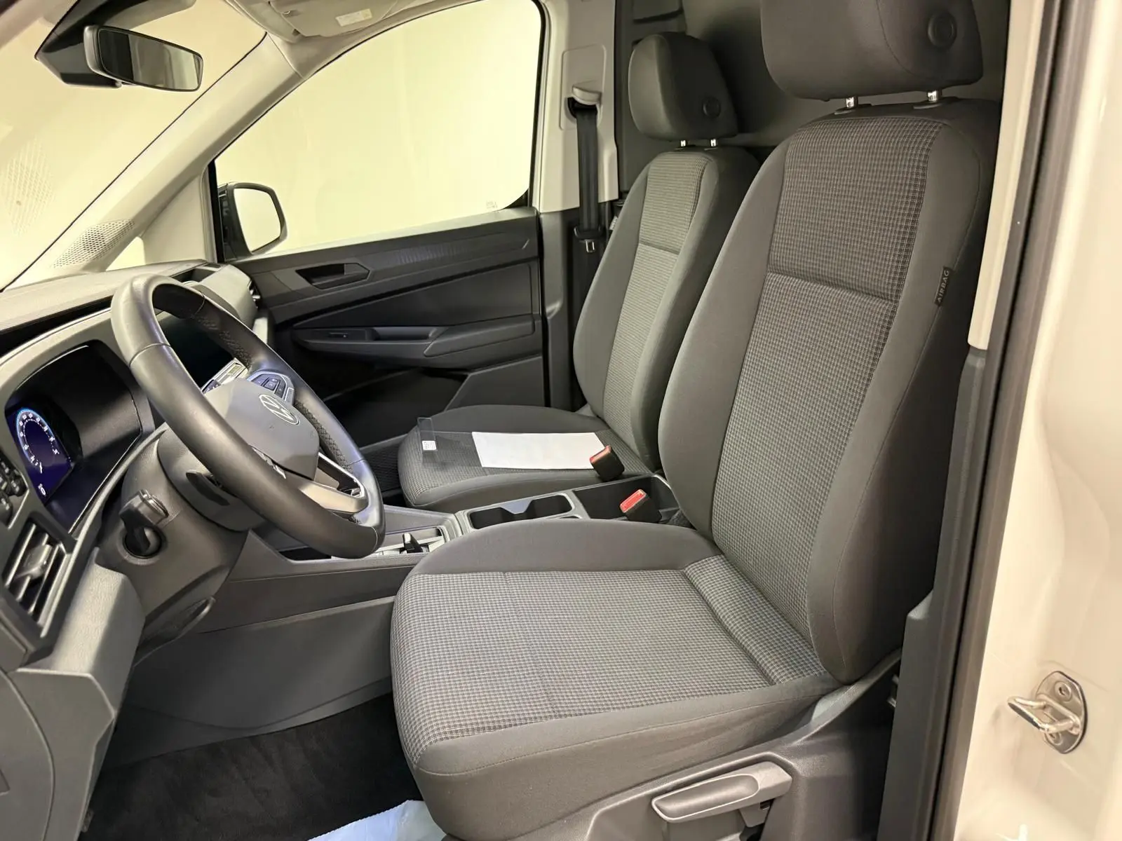 Vue intérieure côté conducteur du Volkswagen Caddy blanc Candy 2025, sièges gris et tableau de bord moderne.