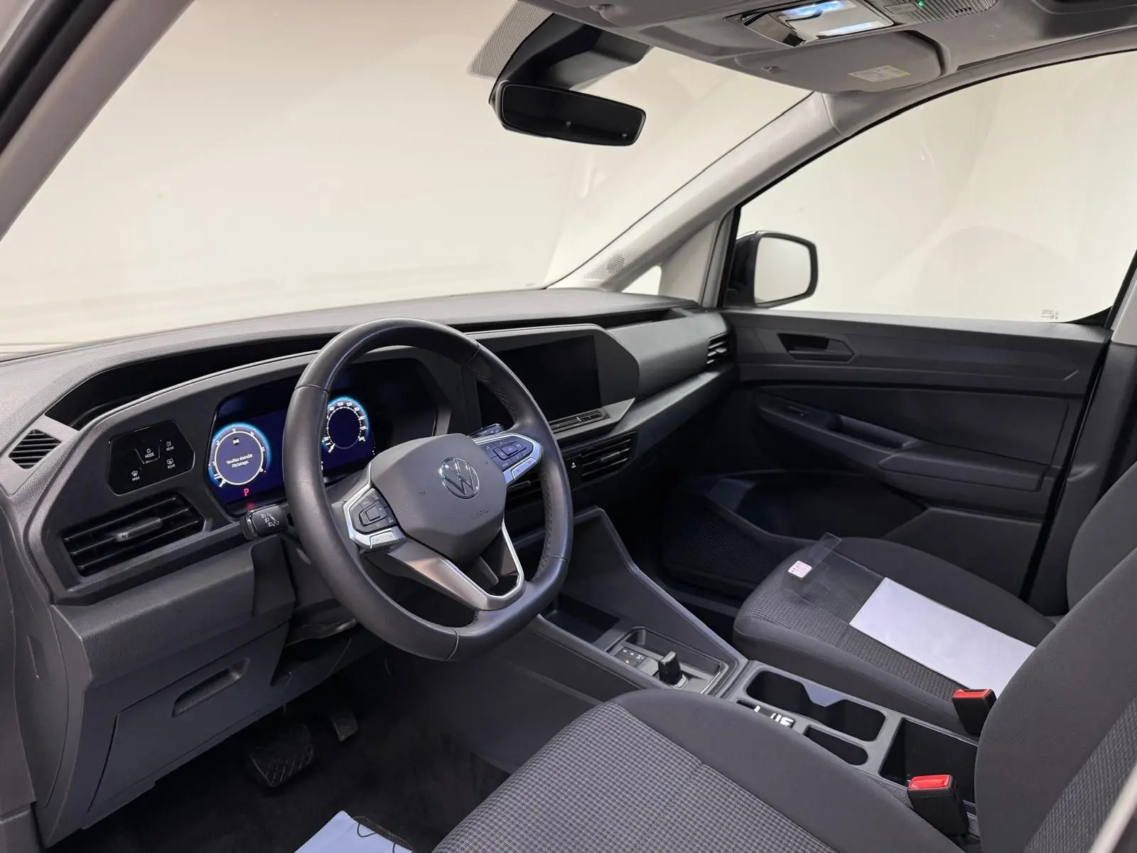 Vue intérieure côté conducteur du Volkswagen Caddy 2025, tableau de bord noir avec volant cuir et écran digital.