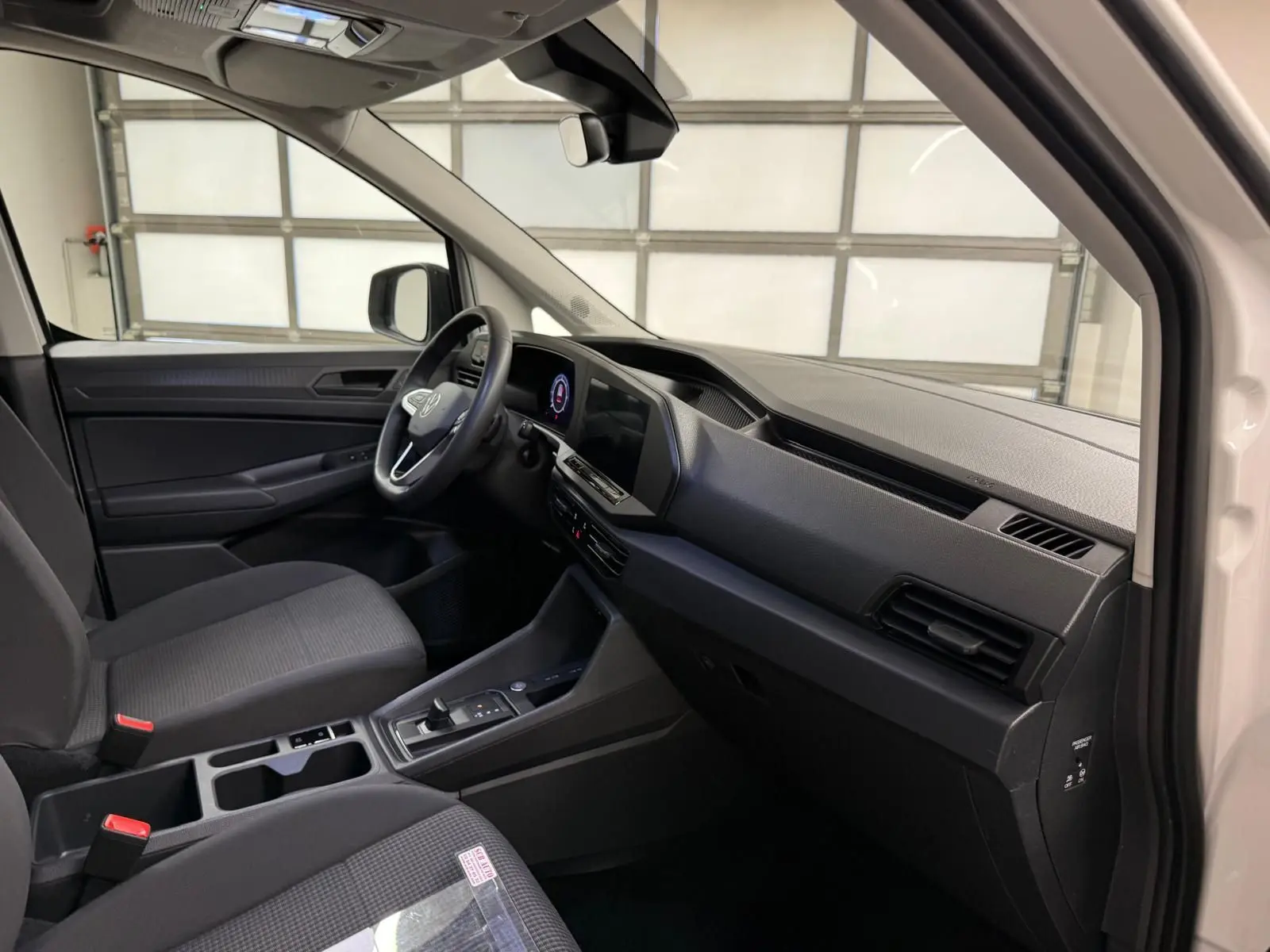 Vue intérieure côté conducteur du Volkswagen Caddy blanc Candy 2025, tableau de bord et console centrale noirs.