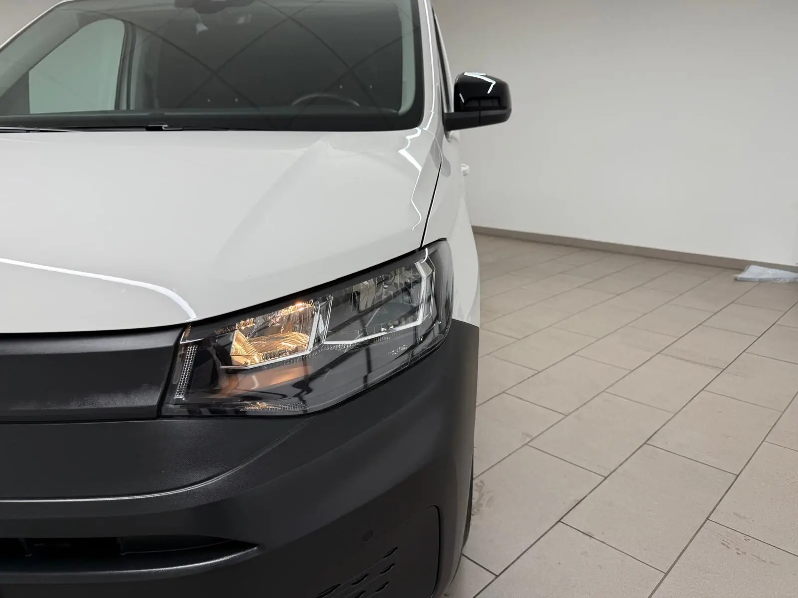 Vue de face droite du Volkswagen Caddy blanc Candy avec phare avant allumé et pare-chocs noir mat.