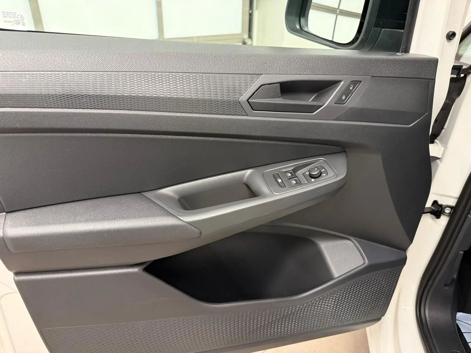Vue rapprochée de la porte avant droite du Volkswagen Caddy blanc Candy, avec commandes électriques et poignée intégrée.