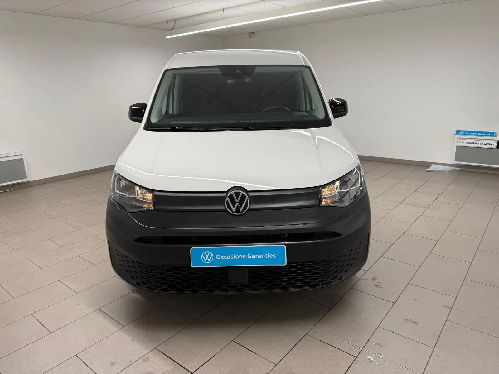Vue de face du Volkswagen Caddy blanc Candy 2025 avec pare-chocs noir mat et logo VW central.