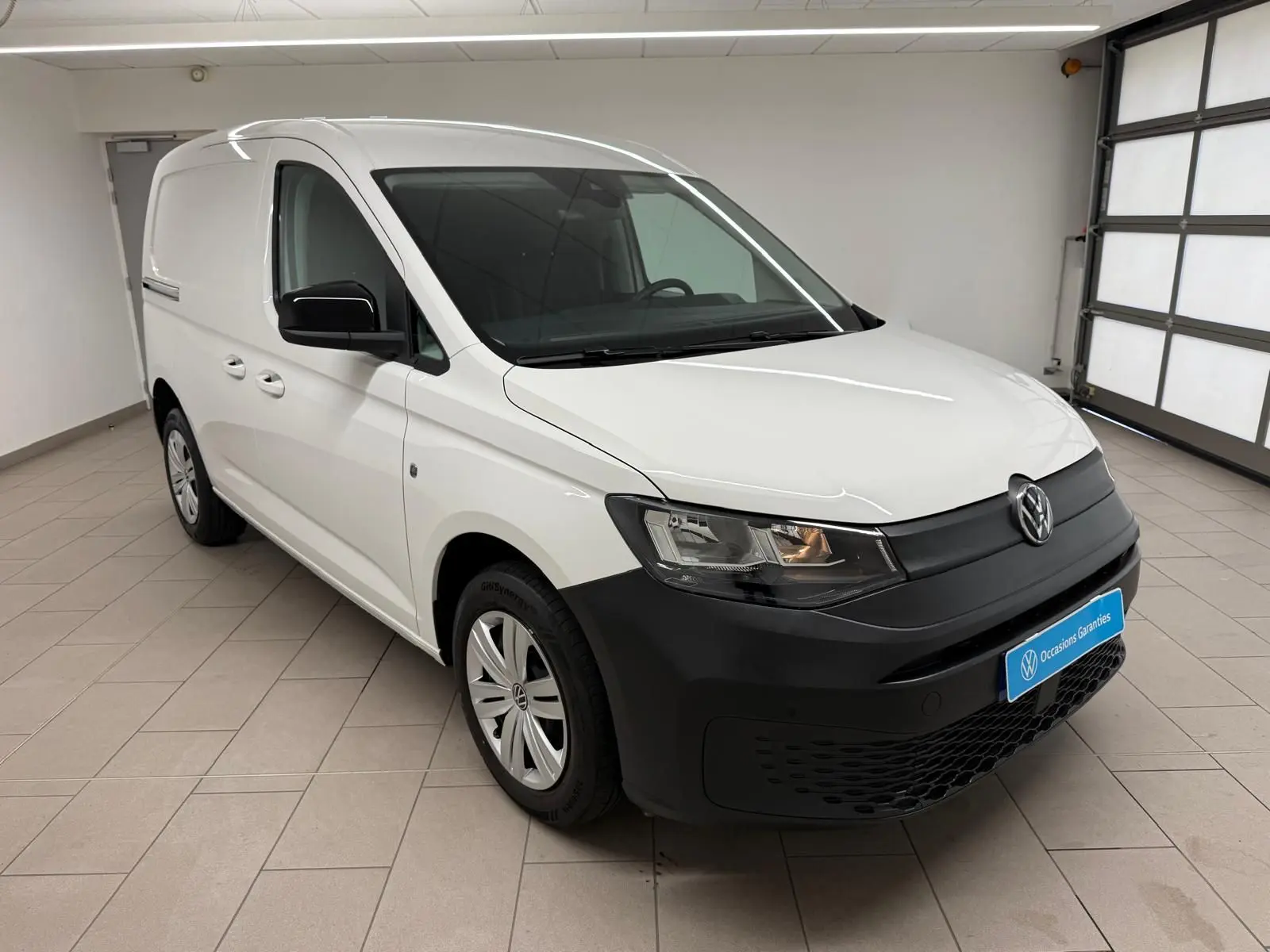 Volkswagen Caddy blanc candy vue 3/4 avant droit avec pare-chocs noir mat et jantes acier 16 pouces.
