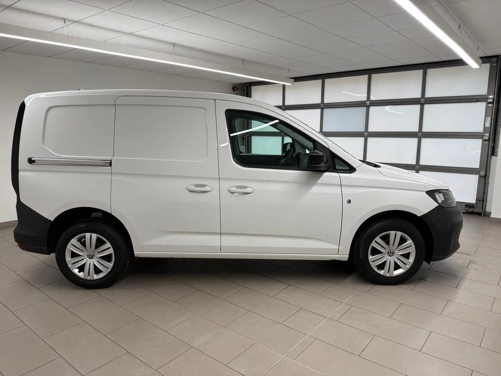 Vue de profil droit du Volkswagen Caddy blanc Candy 2025 avec pare-chocs noirs et jantes acier.