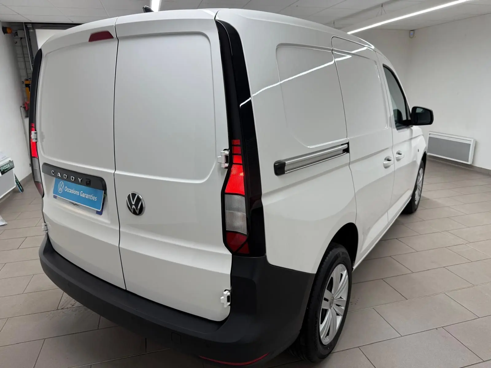 Vue 3/4 arrière droite d'un Volkswagen Caddy blanc Candy avec portes battantes arrière et pare-chocs noir mat.