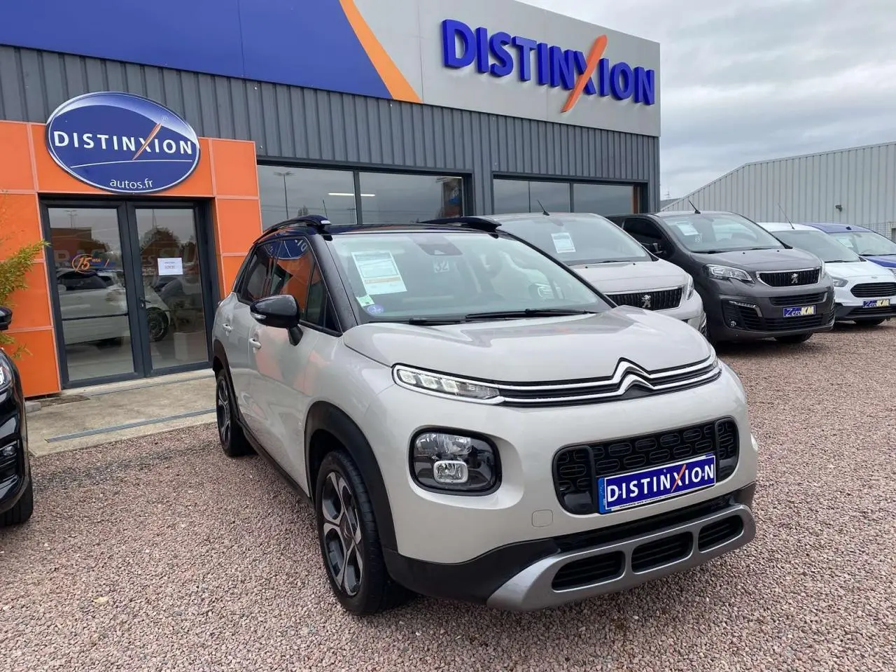 Citroën C3 Aircross grise vue 3/4 avant avec toit noir et détails noirs autour des phares, devant un concessionnaire.