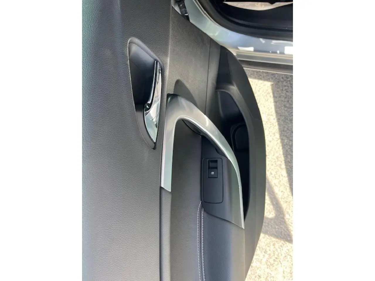 Gros plan sur la poignée intérieure chromée et la commande de verrouillage de la porte côté avant droit d’une Opel Insignia Sports Tourer gris clair.