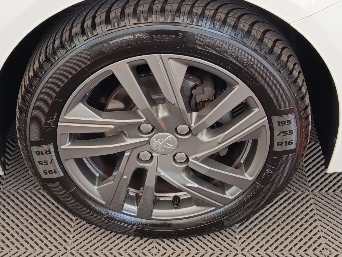 Gros plan sur la roue avant droite d'une Peugeot 208 blanche, avec jante alliage grise et pneu toutes saisons.