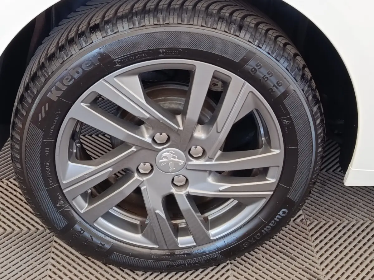 Gros plan sur la roue avant droite d'une Peugeot 208 blanche, avec jante alliage et logo lion au centre.