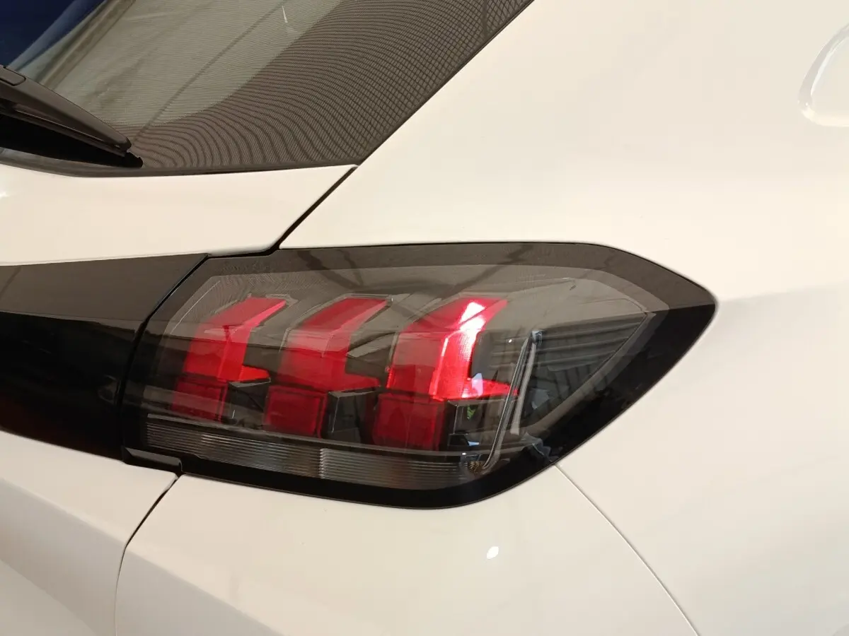 Gros plan sur le feu arrière droit rouge et noir d’une Peugeot 208 blanche vue de l’arrière.