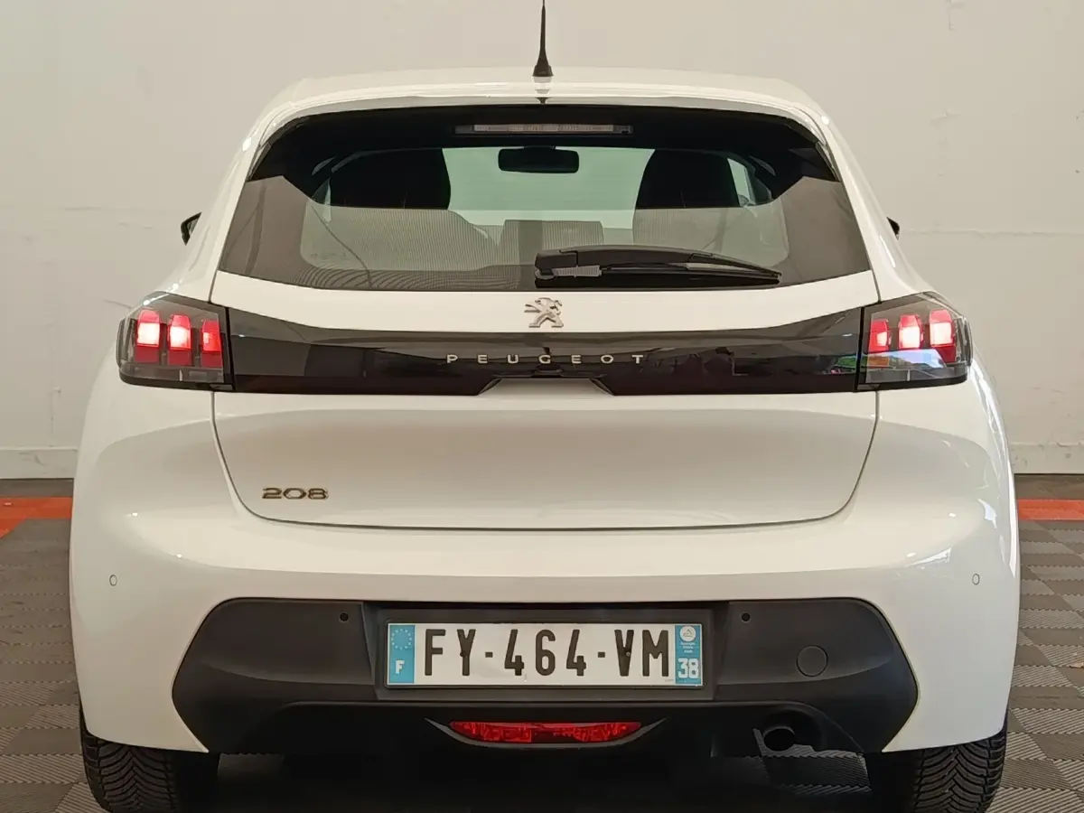 Vue arrière d'une Peugeot 208 blanche avec feux arrière allumés et bande noire distinctive entre les feux.