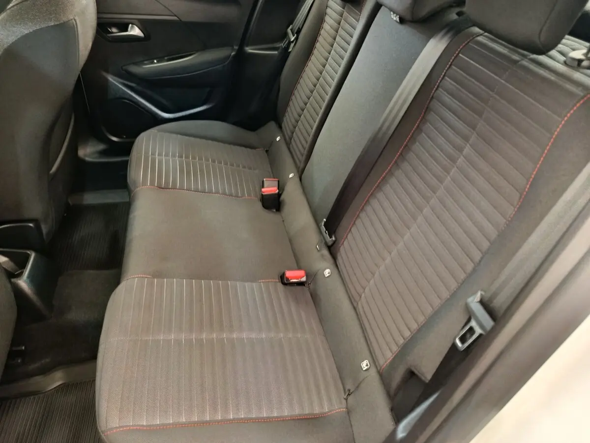 Vue intérieure côté droit montrant la banquette arrière noire avec surpiqûres rouges de la Peugeot 208 blanche.