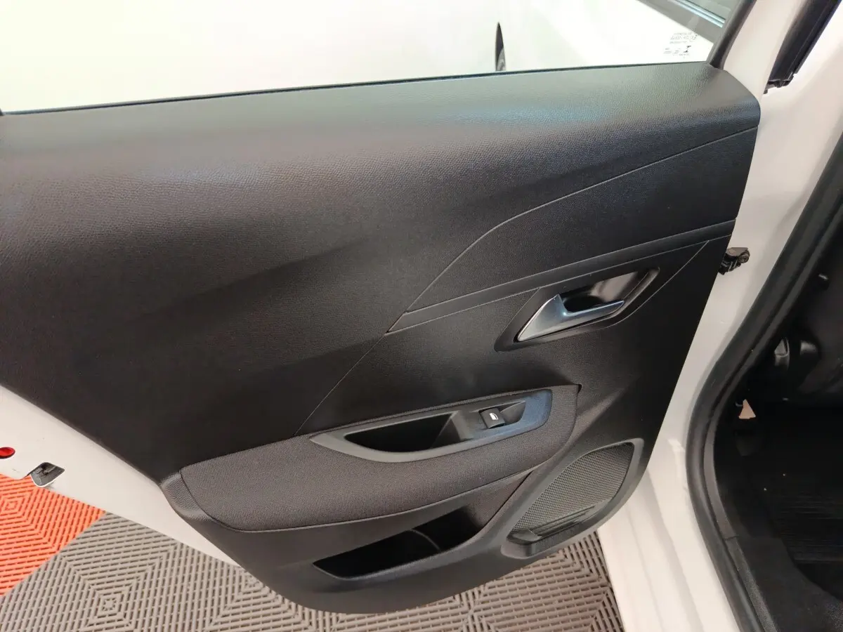 Vue rapprochée de la porte avant droite noire de la Peugeot 208 blanche, montrant la poignée et le bouton de lève-vitre.