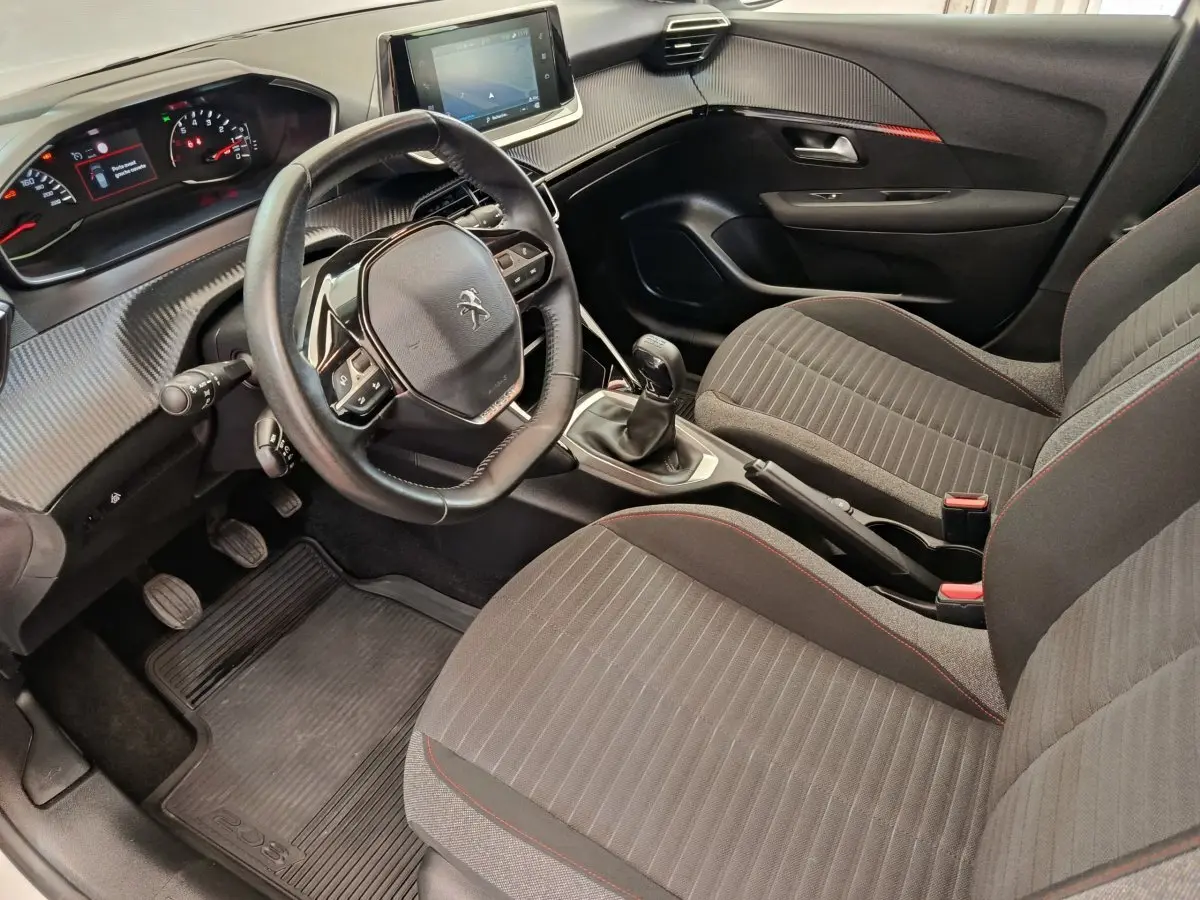 Vue intérieure côté conducteur de la Peugeot 208 blanche, volant cuir multifonctions et écran tactile central visible.