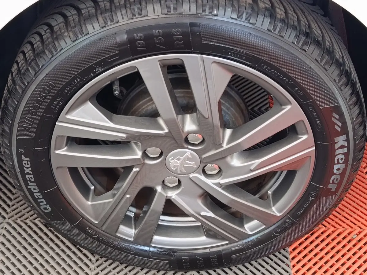 Gros plan sur la jante alliage grise et pneu Kleber d'une Peugeot 208 blanche, vue côté roue avant.