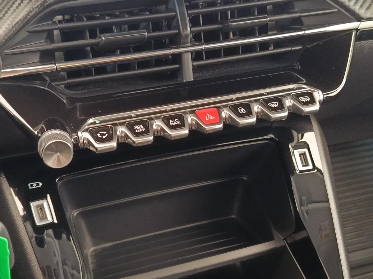 Détail du tableau de bord noir brillant de la Peugeot 208 PureTech 75 avec boutons de commande et ports USB visibles.
