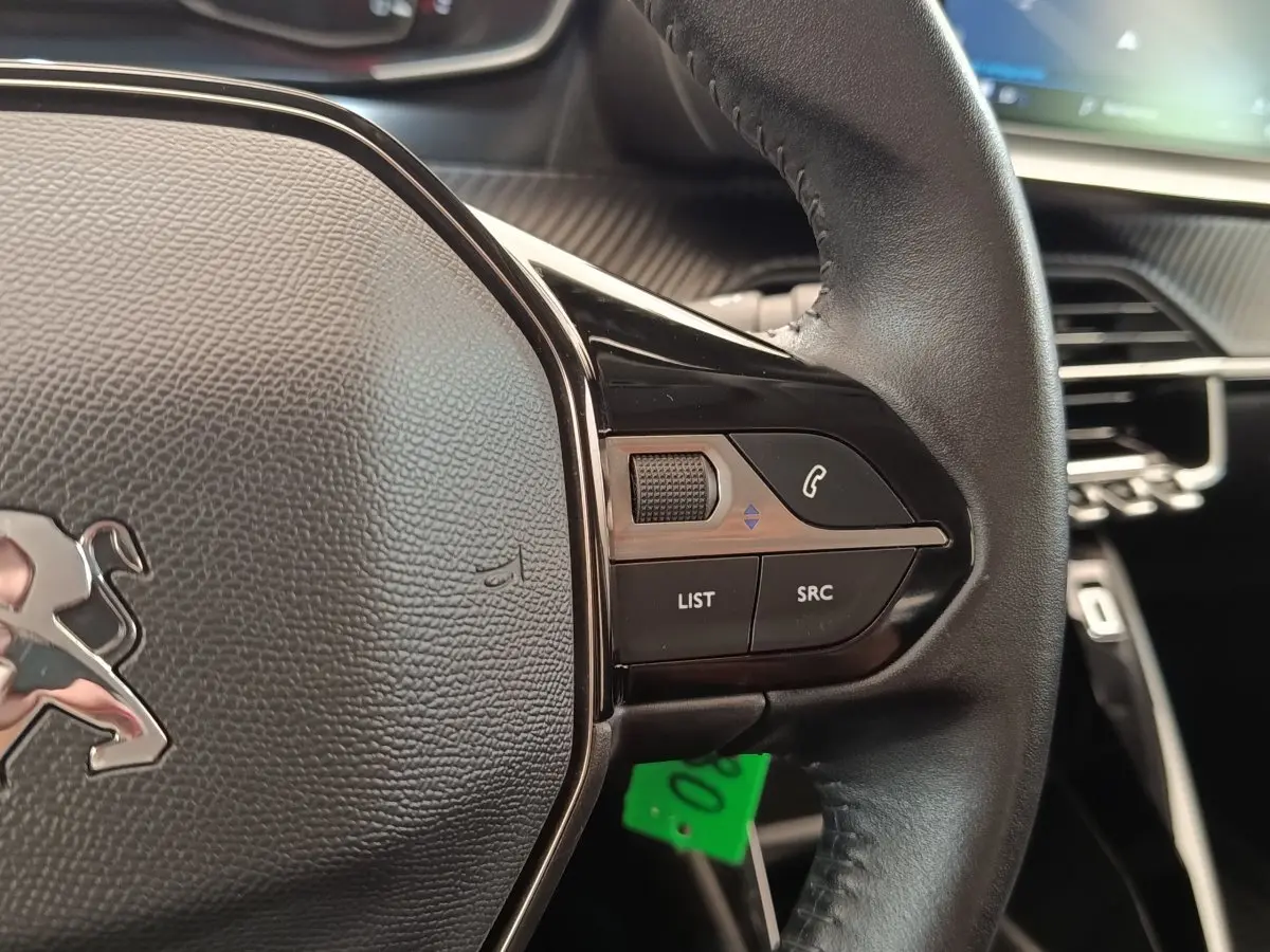 Gros plan sur le volant cuir multifonctions côté droit de la Peugeot 208 blanche, avec commandes audio et téléphone.