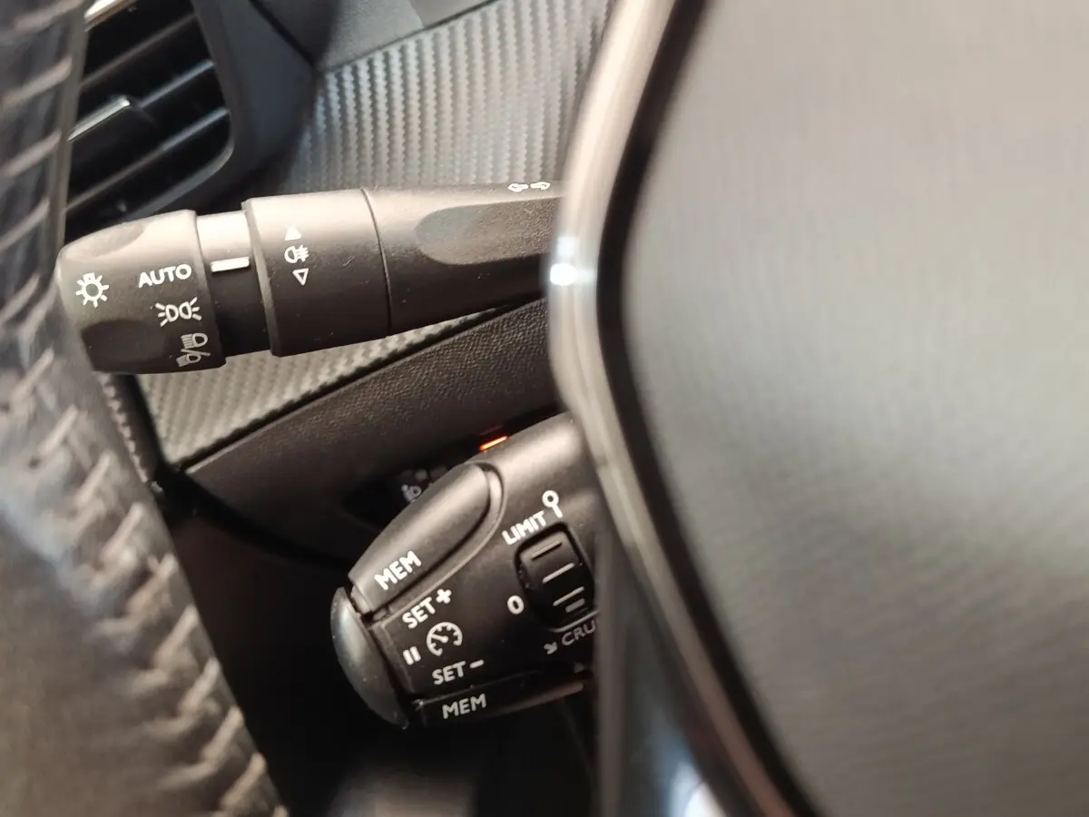 Gros plan sur les commandes de régulateur de vitesse et éclairage derrière le volant cuir d'une Peugeot 208 blanche.