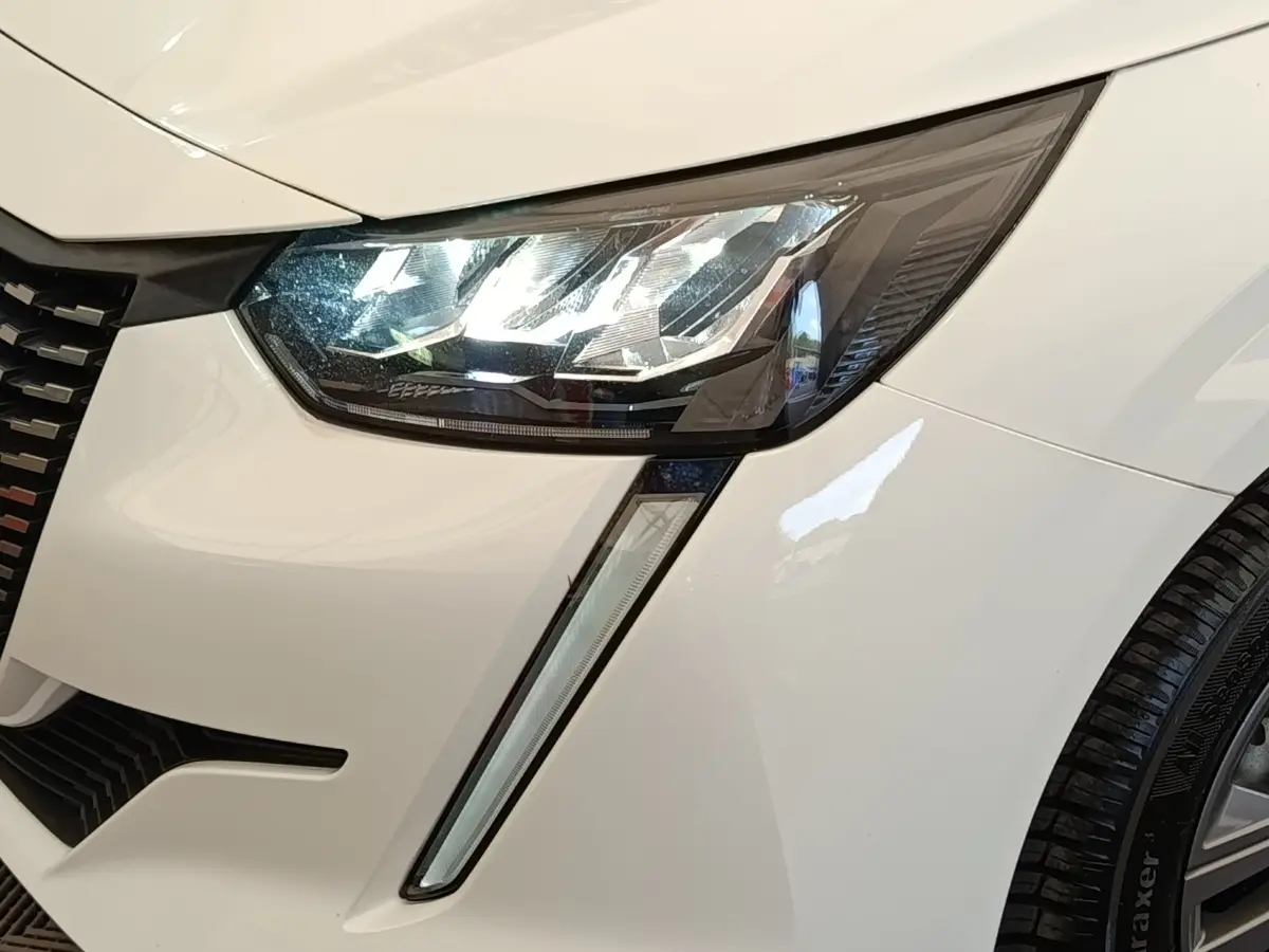 Gros plan sur le phare avant droit blanc d’une Peugeot 208 PureTech 75 S&S Active Business 2021 avec feux LED et calandre noire.
