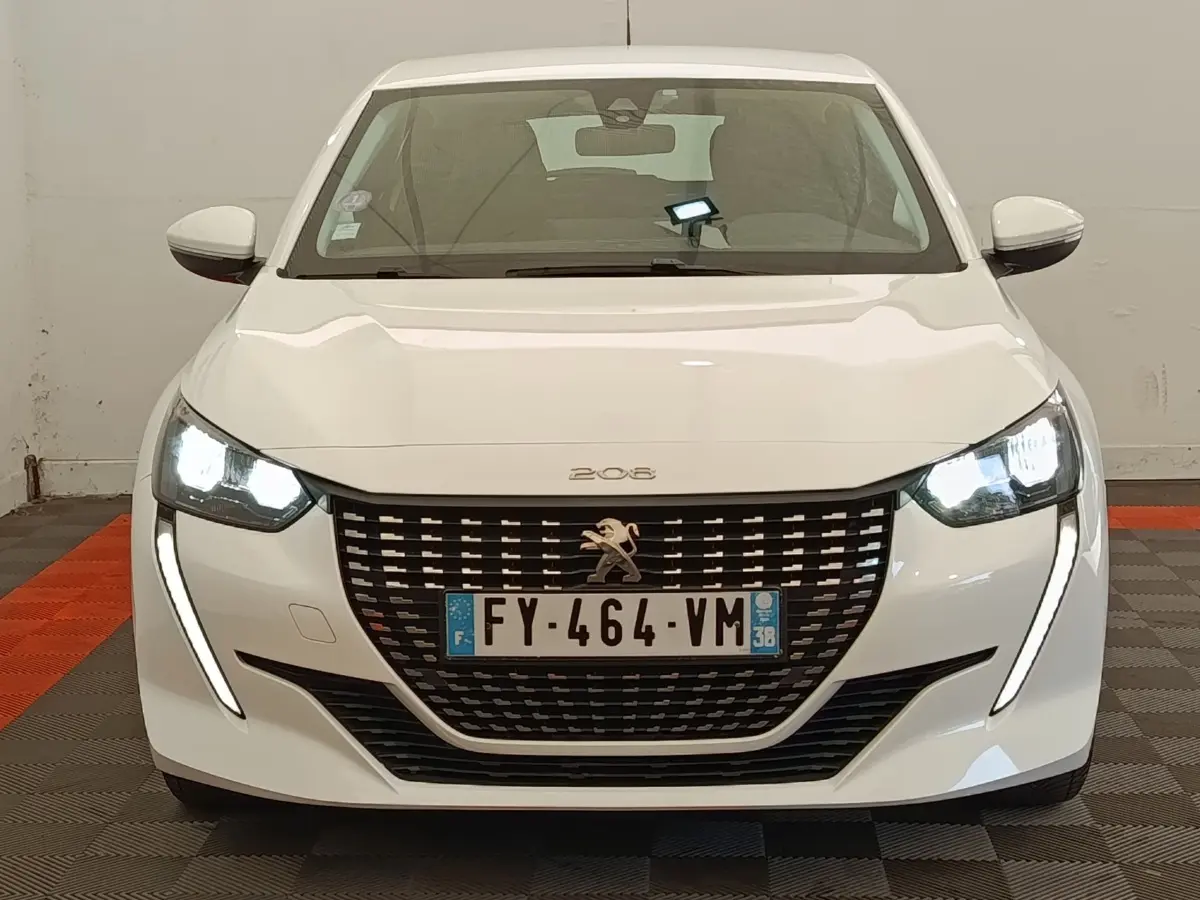Vue avant d'une Peugeot 208 blanche de 2021 avec phares LED allumés et calandre noire distinctive.