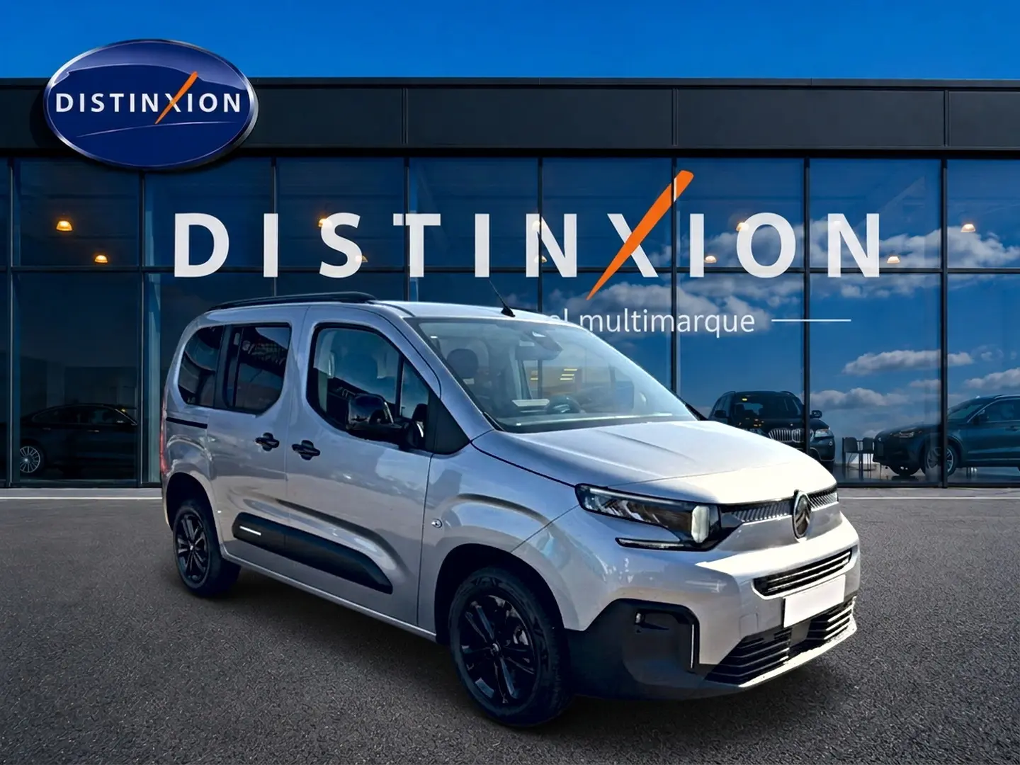 Vue 3/4 avant du Citroën Berlingo Steel Grey 2026 avec barres de toit et jantes noires devant un showroom.
