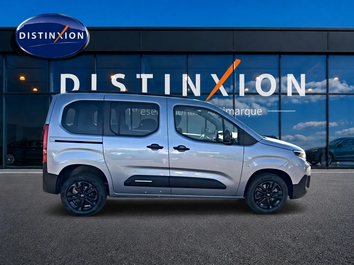 Profil droit du Citroën Berlingo 2026 steel grey avec barres de toit et jantes noires devant une vitrine Distinxion.
