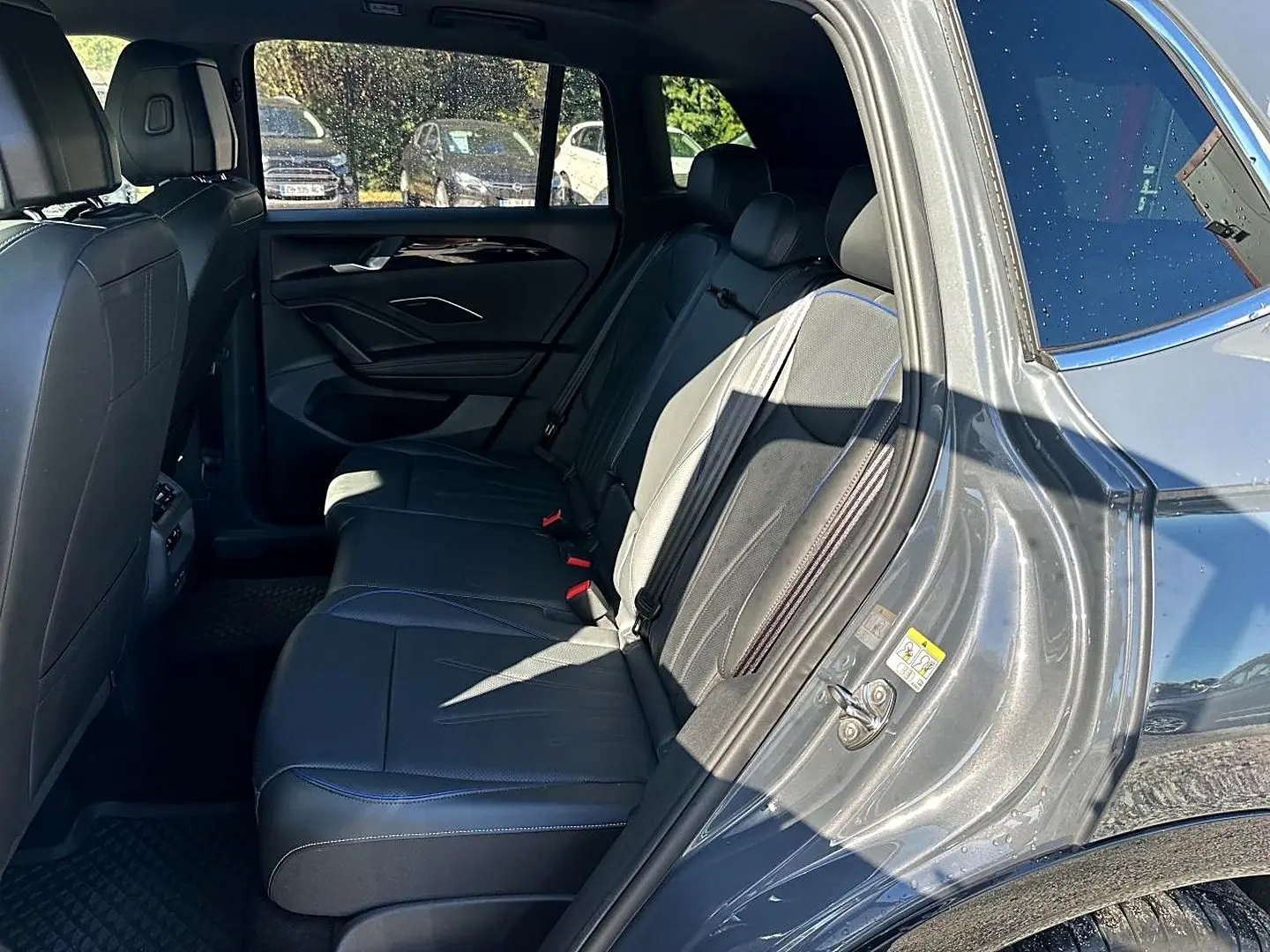 Vue intérieure côté arrière droit du Volkswagen Tiguan gris dauphin 2024, sièges en cuir noir avec surpiqûres bleues.