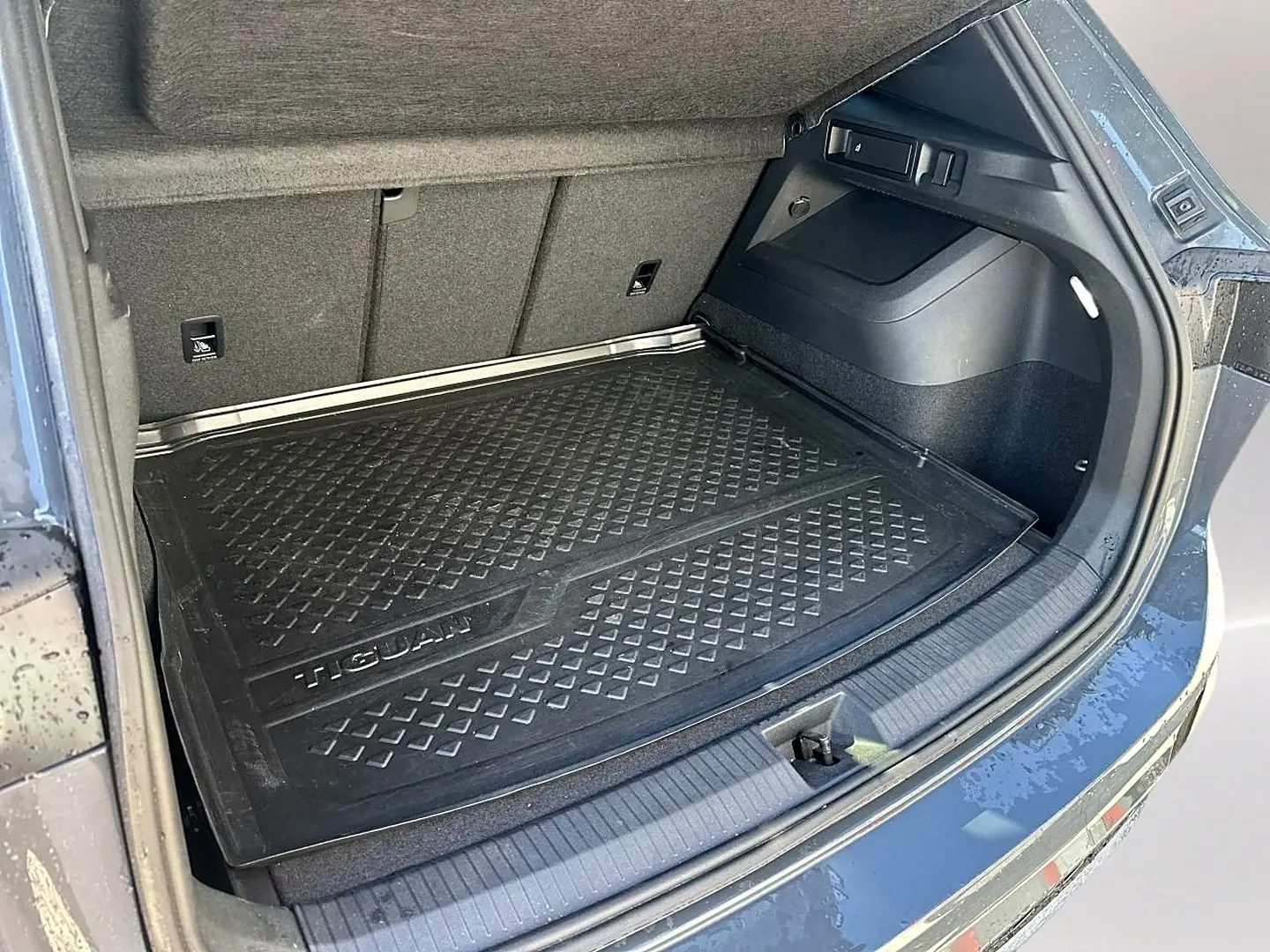Coffre ouvert du Volkswagen Tiguan gris dauphin 2024, avec tapis de protection noir marqué Tiguan visible.