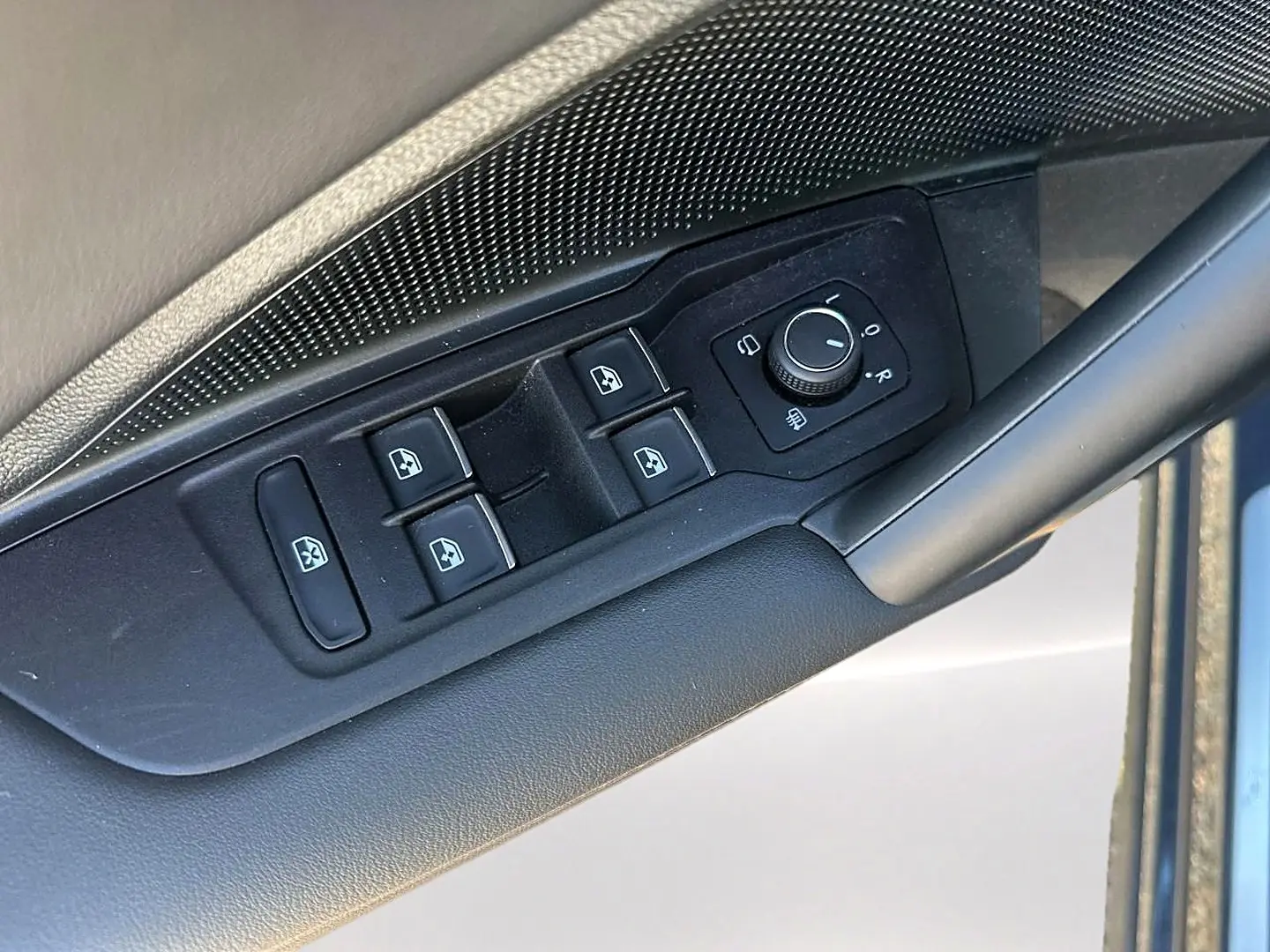 Gros plan sur les commandes de lève-vitres et réglage des rétroviseurs côté conducteur du Volkswagen Tiguan gris dauphin.