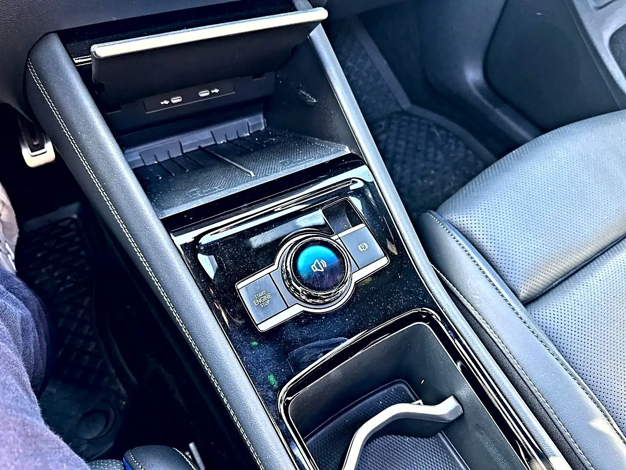Vue rapprochée de la console centrale noire brillante du Volkswagen Tiguan 2024 avec accoudoir et siège en cuir gris.