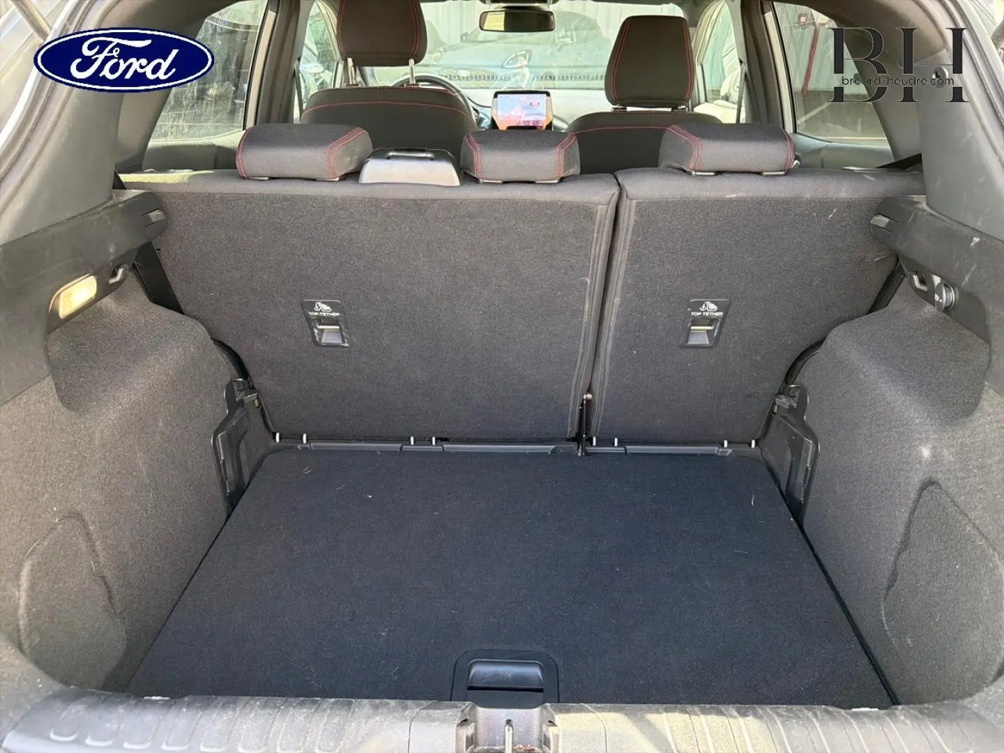 Coffre ouvert de Ford Puma 2024 gris Solar Métallisé, vue arrière montrant banquette arrière avec surpiqûres rouges.
