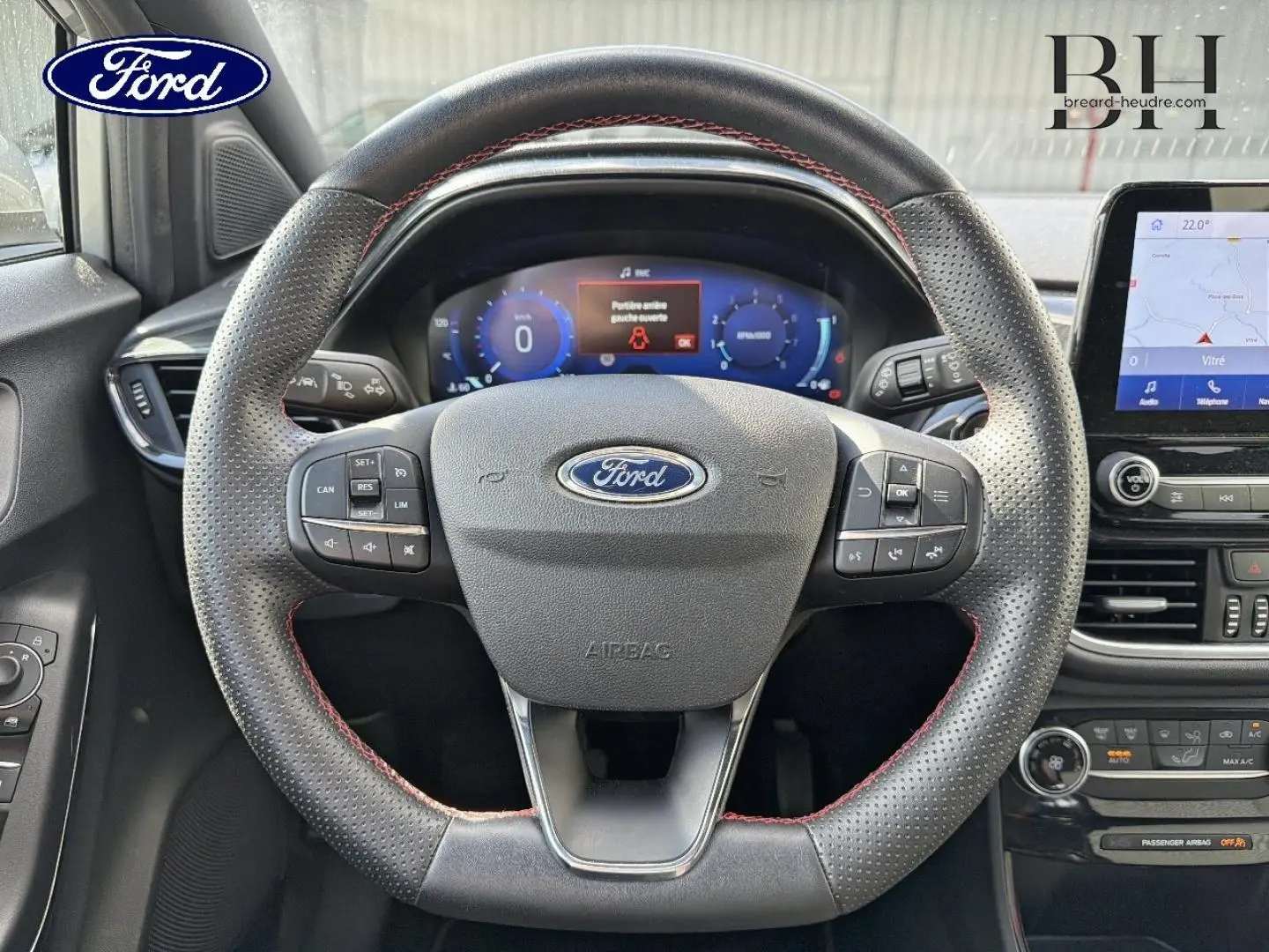 Vue intérieure centrée sur le volant perforé avec surpiqûres rouges du Ford Puma 2024 gris Solar Métallisée, tableau de bord digital visible.